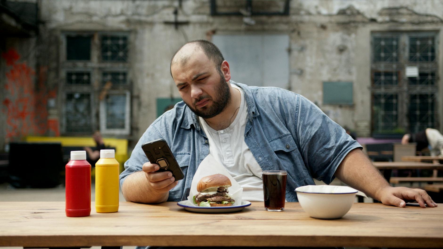 bald man sitting on wooden table looking at his smartphone